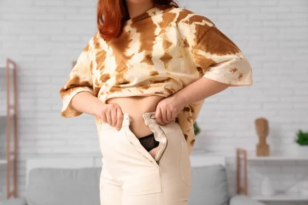 Image of woman trying to do her trousers up after pregnancy weight gain Sutton in Ashfield